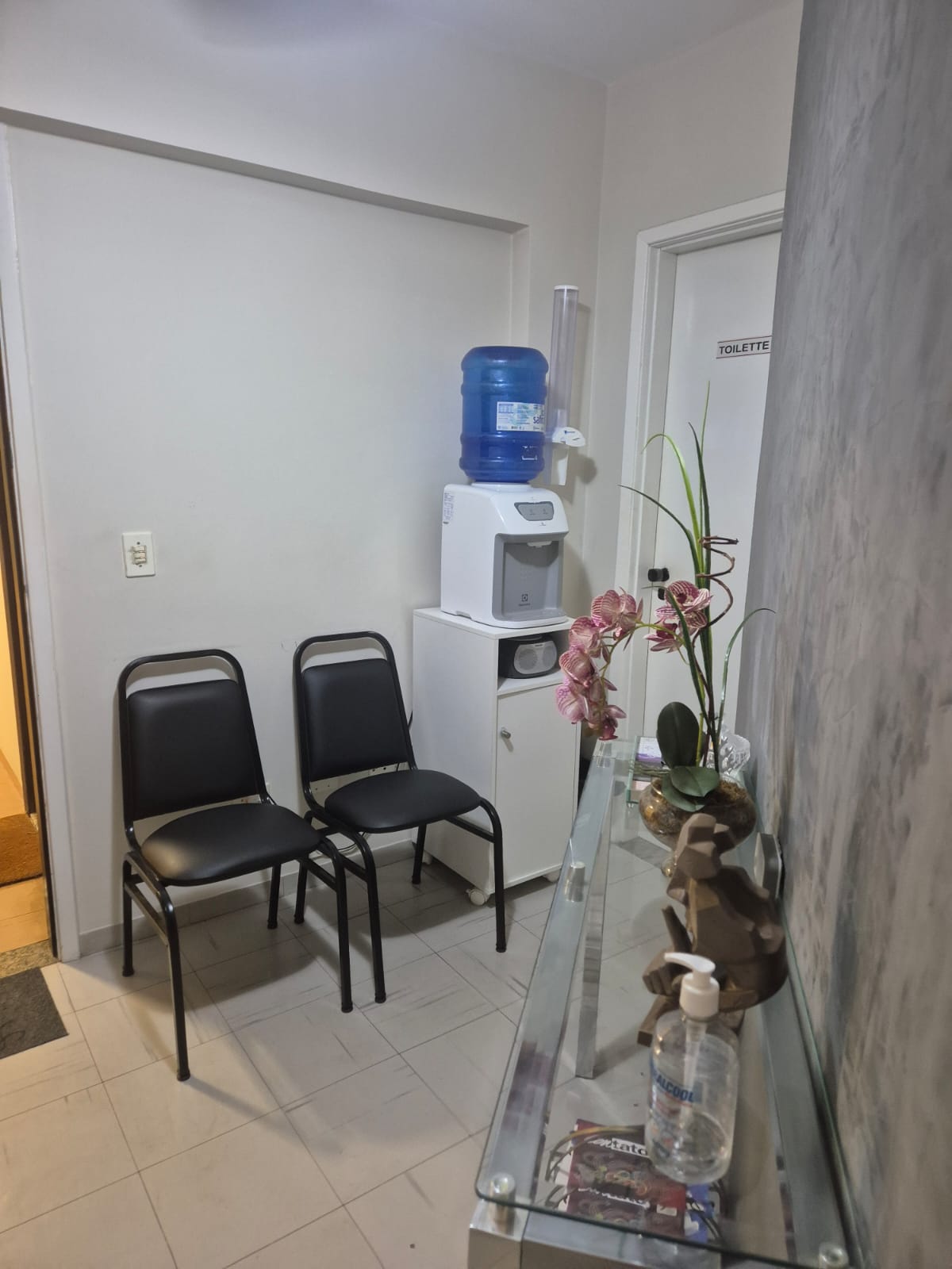 Sala de espera com cadeiras, bebedouro e porta do toilette
